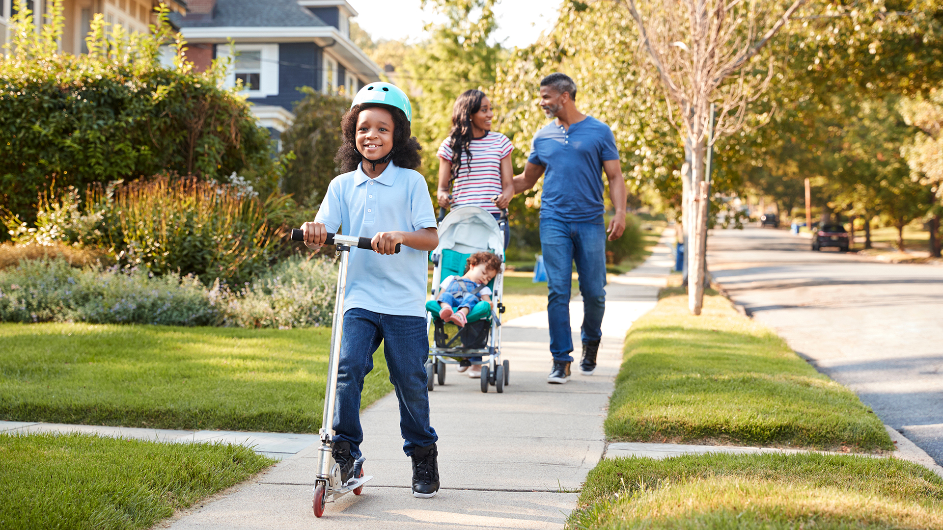 Couple Push Daughter In Stroller As Son Rides Scooter Couple Push Daughter In Stroller As Son Rides Scooter