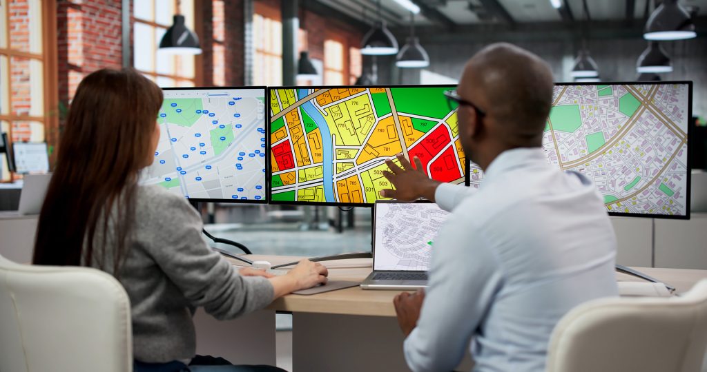 Two GIS Analysts In Office Using Computers To Review Urban Plann